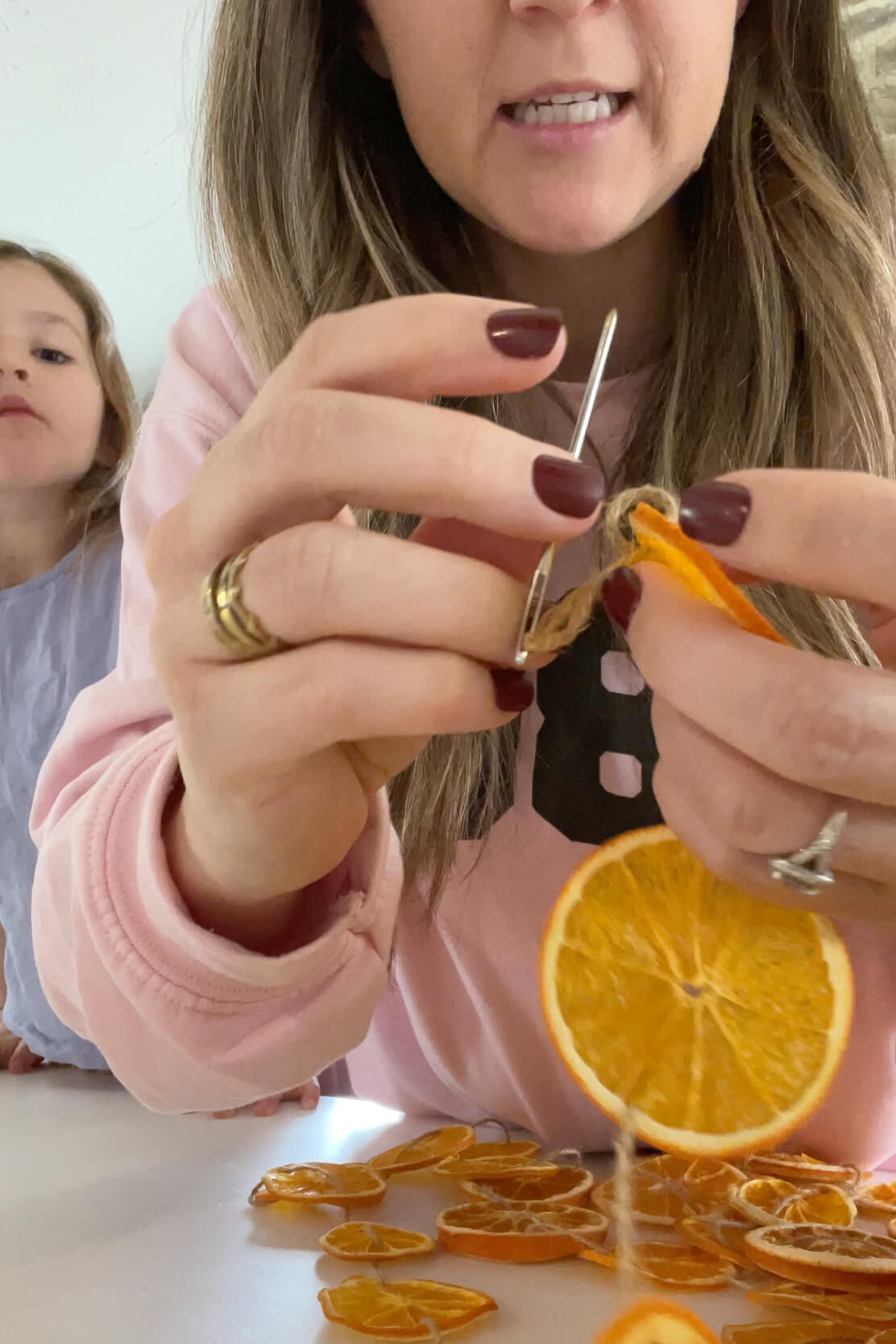 Using a large needle to tie the twine at the end of an orange slice garland.